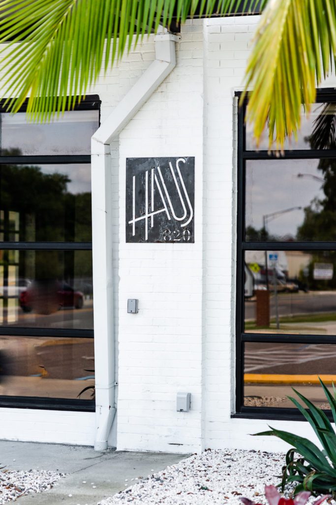 White brick exterior with Haus 820 logo boldly stenciled on the siding. Palm trees gently frame the patio area.