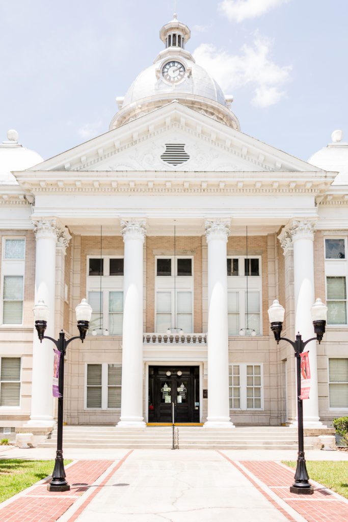 Exterior view of the Old Polk County Courthouse. Corinthian pillars support a beautiful white entryway that is topped by a rotunda