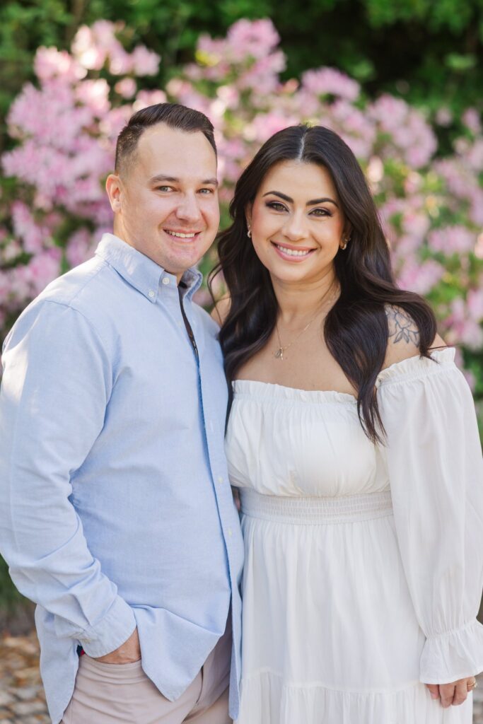 Close portrait of the couple smiling with pink azaleas behind them