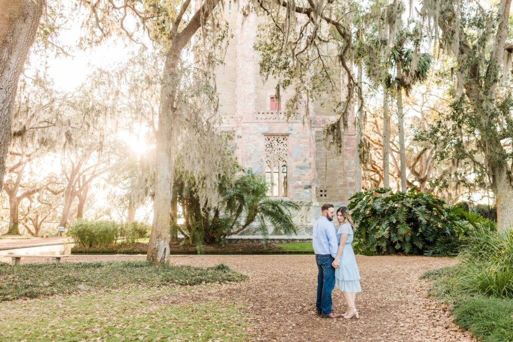 Couple beneath mossy live oaks with the Singing Tower behind them at Bok Tower Gardens