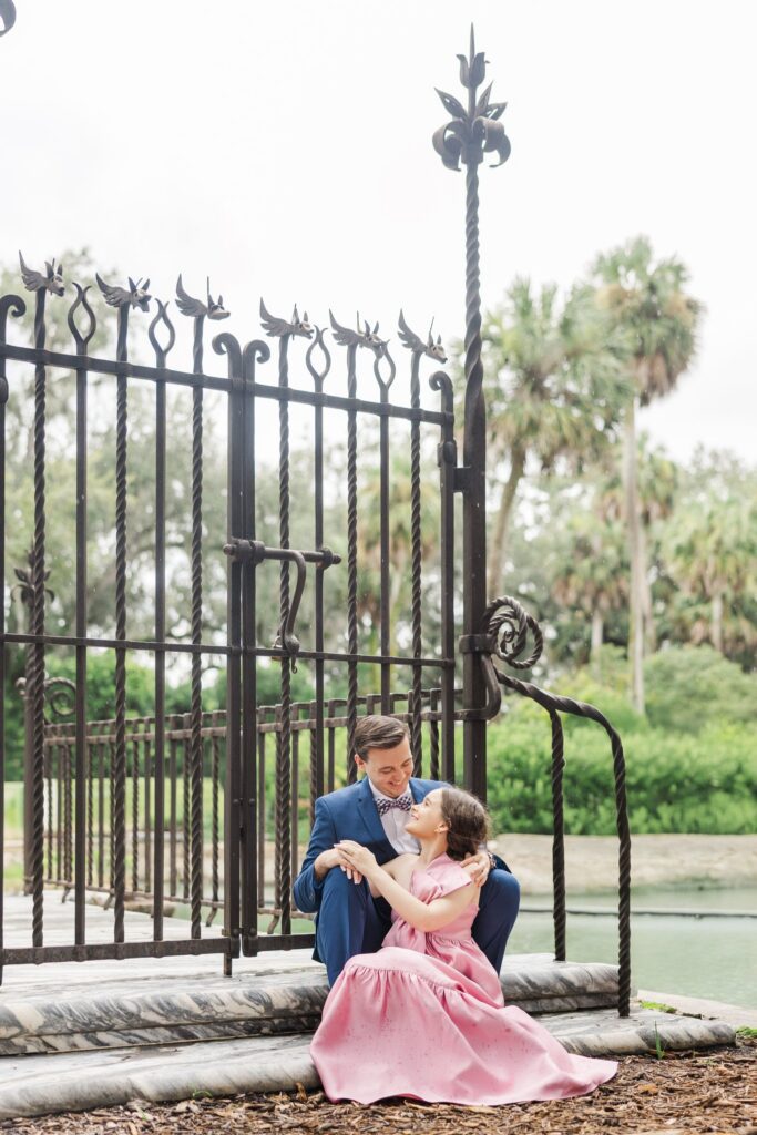 Engaged couple sitting on the steps below Samuel Yellin's wrought iron gates by the moat at Bok Tower Gardens
